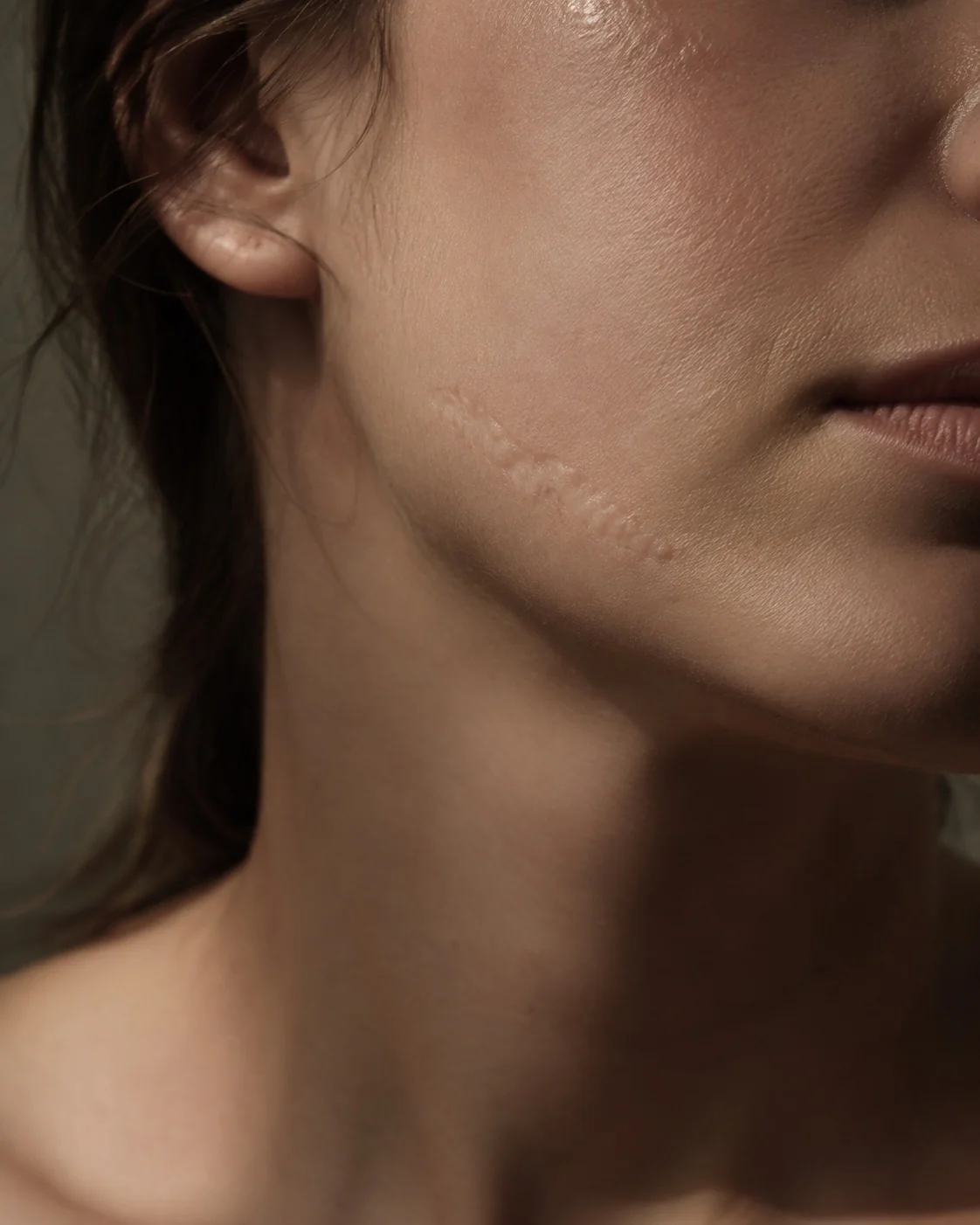 Jawline and lower cheek in steep raking light, scar relief casting shadow.