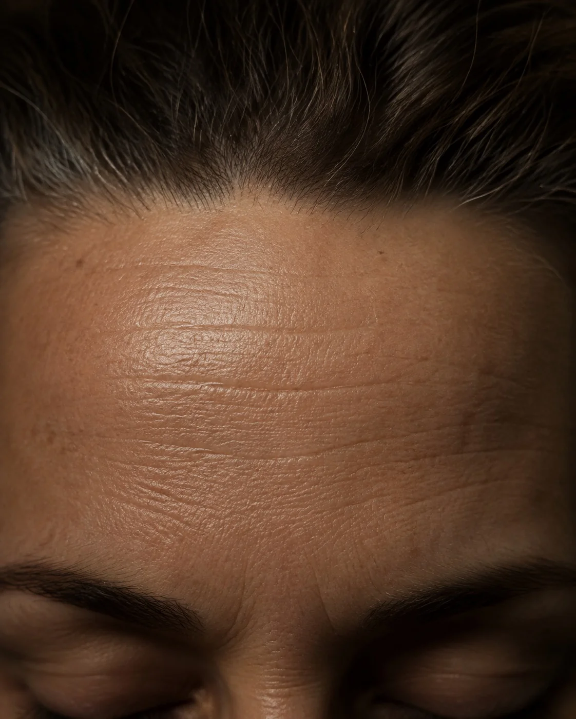 Macro of a forehead at rest, lit from above so fine lines read as topography.